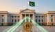 Bank z flagą Pakistanu, przed którym stoi złota moneta Bitcoin z cyfrową siecią powiązań symbolizującą rezerwy kryptowalutowe.
