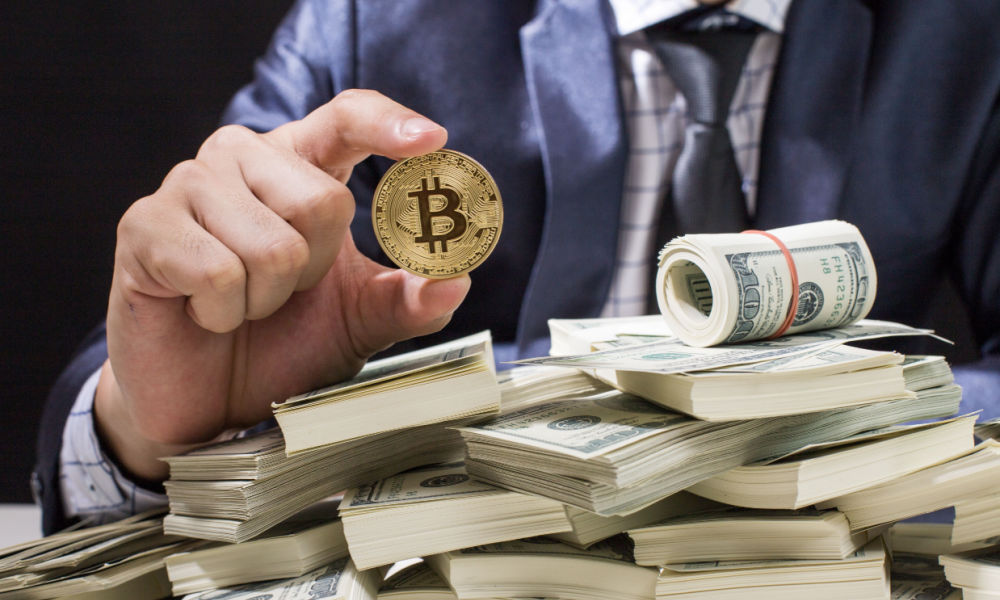 mężczyzna trzymający bitcoina nad pieniędzmi 